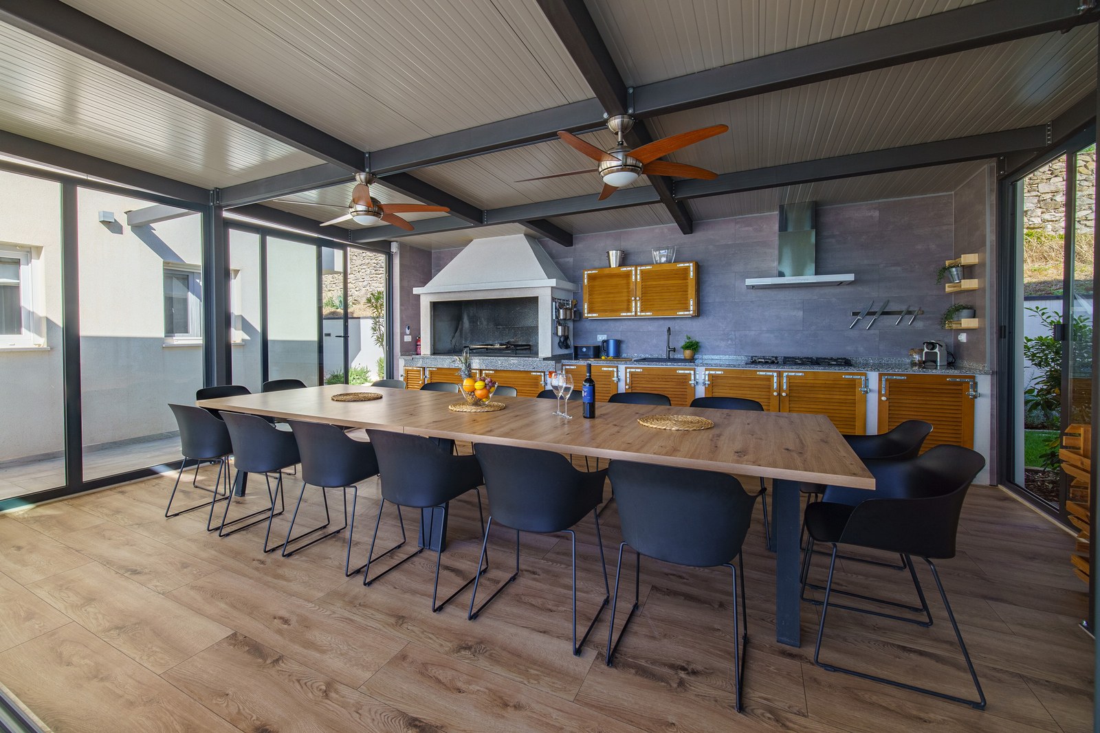 Covered outdoor kitchen with a long group dining table, built-in barbecue and ceiling fans